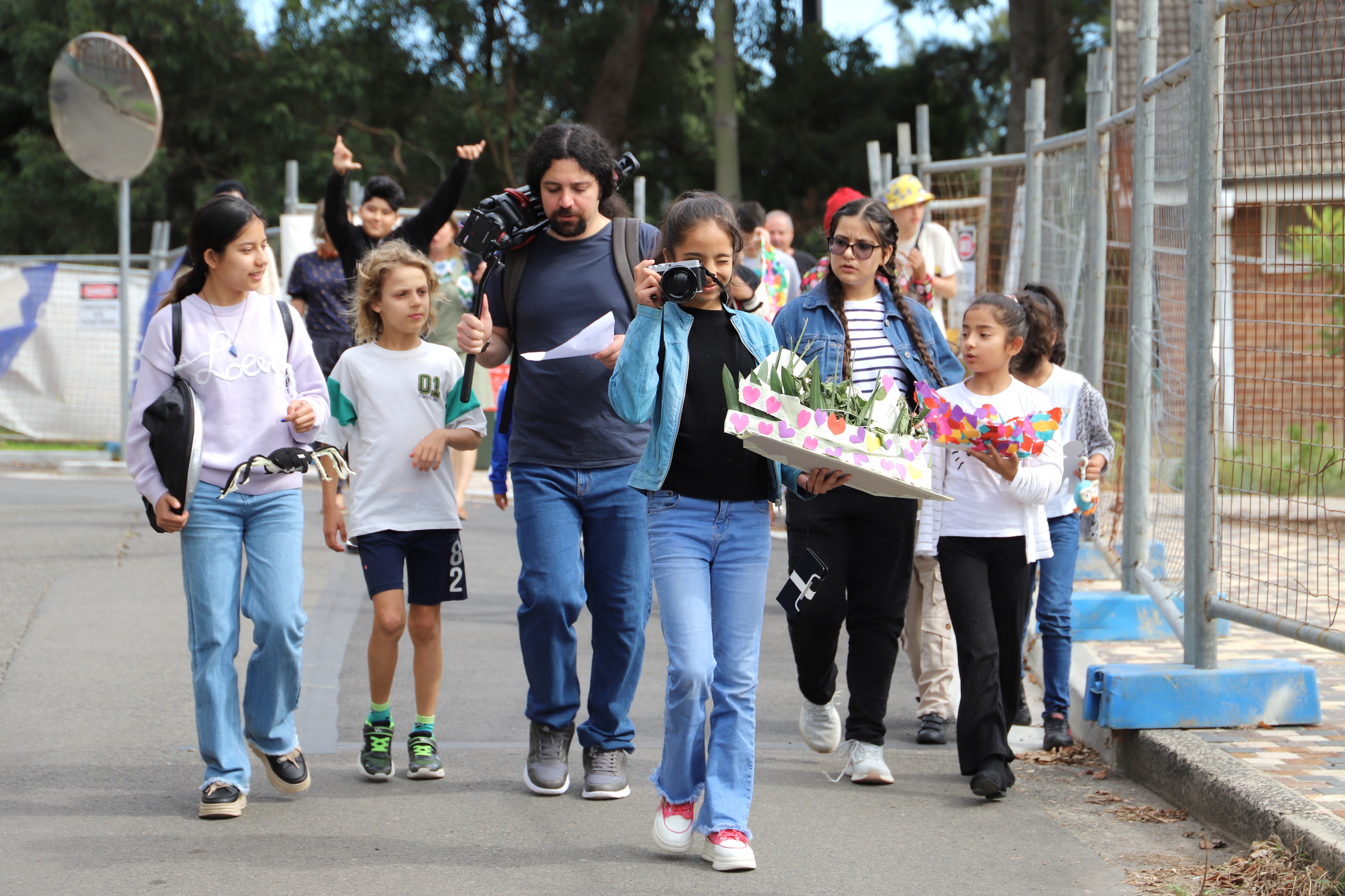 Photo of film participants walking down a street in Callan park, they hold film equipment and one holds a camera up to her eye